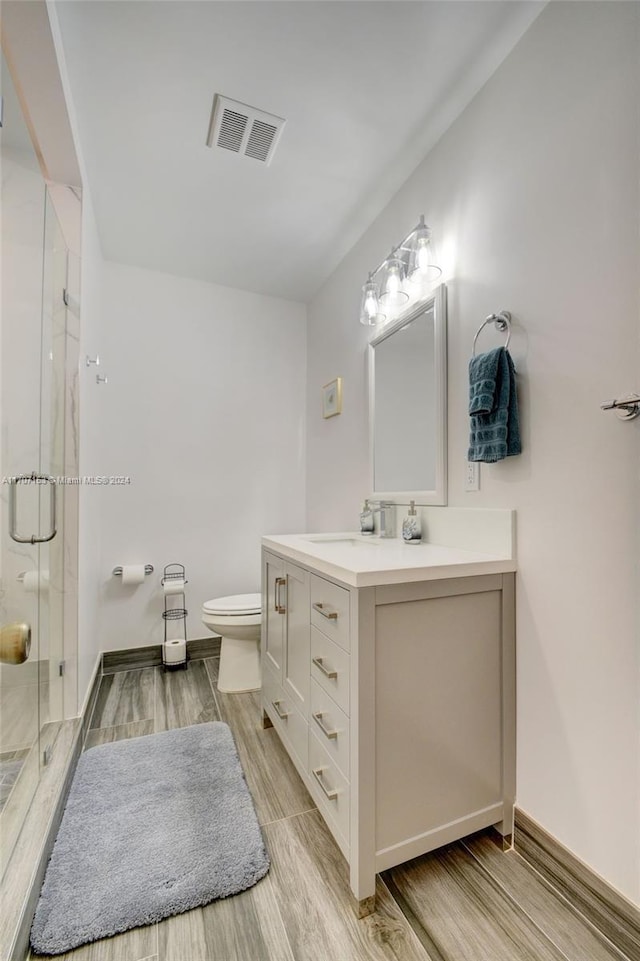 bathroom featuring vanity, wood-type flooring, a shower with shower door, and toilet