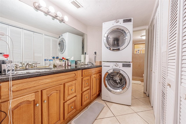 laundry room with a textured ceiling, light tile patterned flooring, stacked washing maching and dryer, and sink