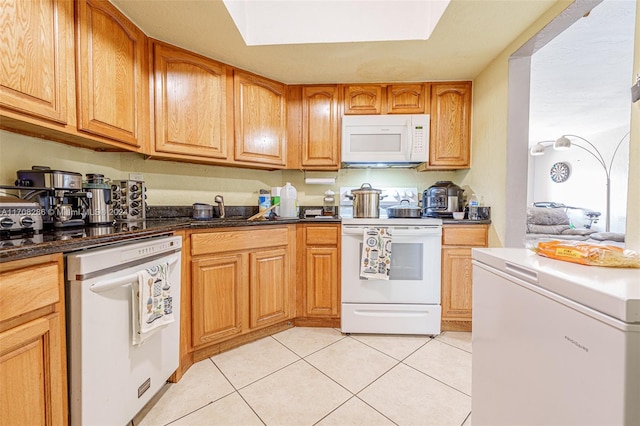 kitchen with sink, light tile patterned floors, dark stone counters, and white appliances