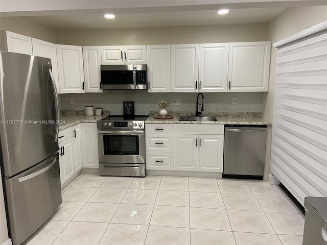 kitchen featuring sink, decorative backsplash, light stone counters, white cabinetry, and stainless steel appliances