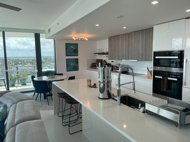 kitchen featuring a breakfast bar, expansive windows, white cabinetry, and black double oven