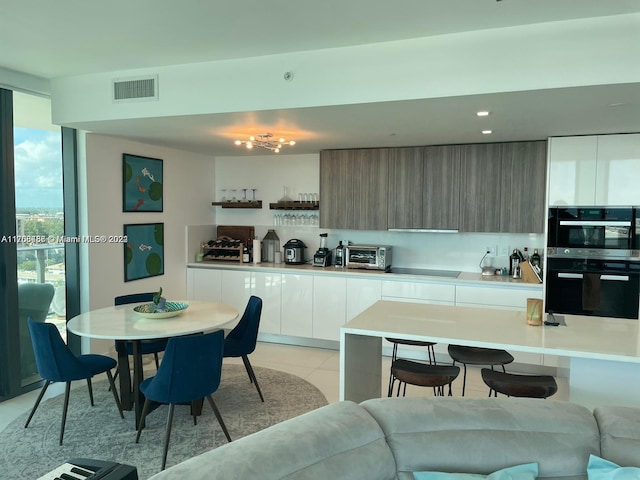 kitchen featuring light tile patterned floors, white cabinetry, a kitchen breakfast bar, and black appliances