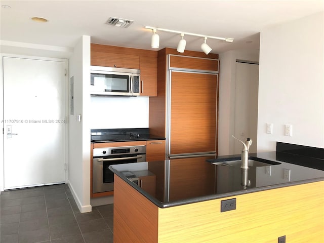 kitchen with rail lighting, sink, dark tile patterned floors, kitchen peninsula, and stainless steel appliances