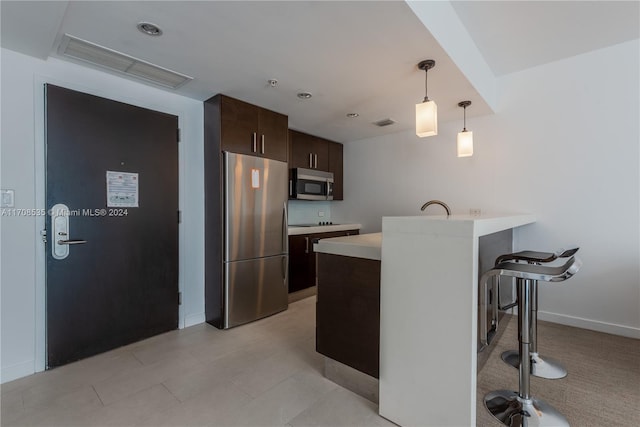 kitchen featuring pendant lighting, dark brown cabinetry, appliances with stainless steel finishes, a kitchen bar, and kitchen peninsula