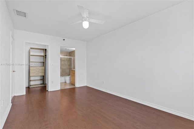 unfurnished bedroom featuring ensuite bathroom, dark hardwood / wood-style floors, a spacious closet, ceiling fan, and a closet