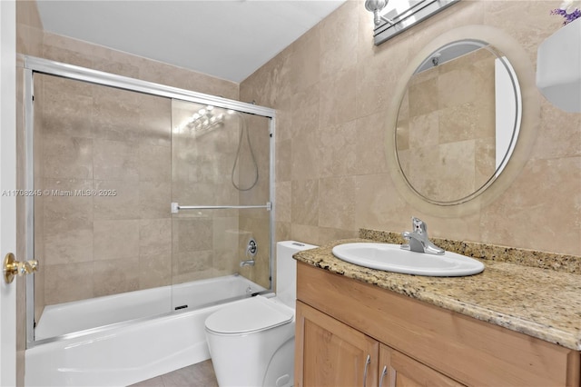 full bathroom with tile walls, vanity, shower / bath combination with glass door, and toilet