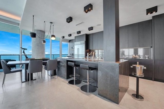 kitchen featuring stainless steel built in fridge, a water view, sink, hanging light fixtures, and light stone counters