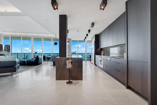 kitchen with white oven, a water view, expansive windows, and a center island with sink