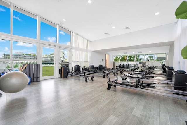 gym featuring light wood-type flooring, a towering ceiling, and a wall of windows