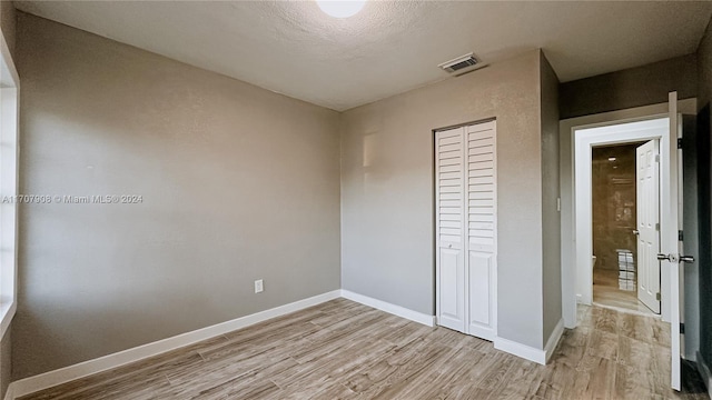 unfurnished bedroom with a textured ceiling, light hardwood / wood-style flooring, and a closet