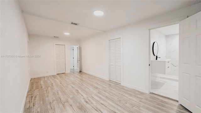 unfurnished bedroom featuring light wood-type flooring, ensuite bath, and multiple closets