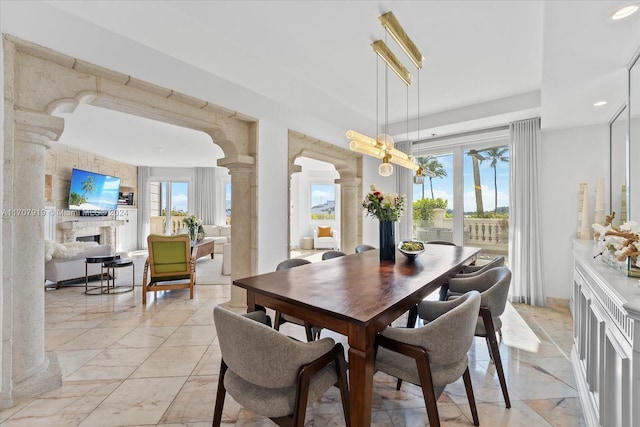 dining room featuring decorative columns, a fireplace, and a healthy amount of sunlight