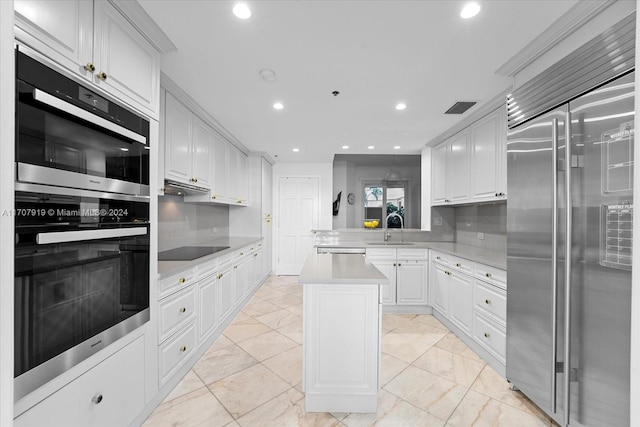 kitchen featuring black appliances, sink, tasteful backsplash, a kitchen island, and white cabinetry