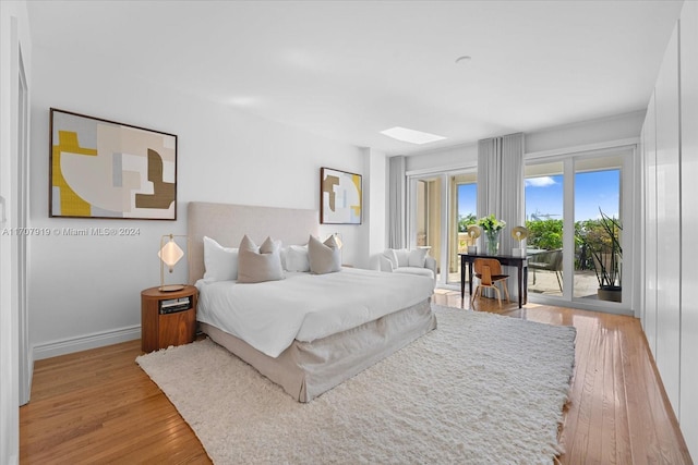 bedroom with access to outside, a skylight, and light hardwood / wood-style flooring