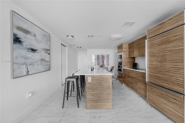 kitchen with a kitchen breakfast bar, a kitchen island with sink, sink, and appliances with stainless steel finishes