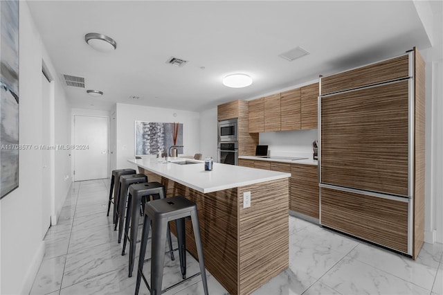 kitchen with sink, a kitchen bar, a kitchen island with sink, and stainless steel appliances