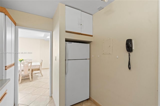 kitchen with white cabinets, electric panel, white fridge, and light tile patterned flooring