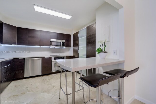 kitchen with decorative backsplash, dark brown cabinets, stainless steel appliances, and a breakfast bar area