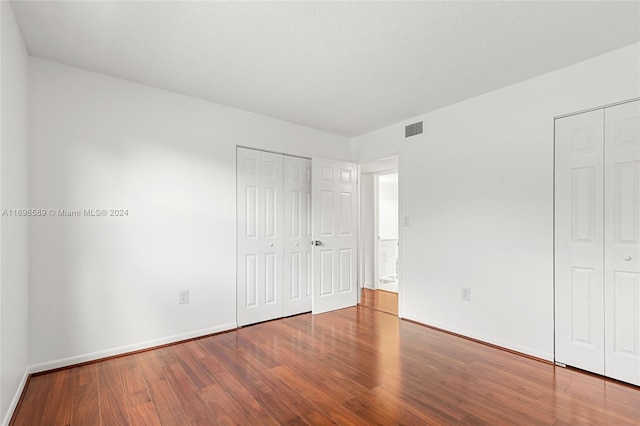 unfurnished bedroom with wood-type flooring, a textured ceiling, and two closets