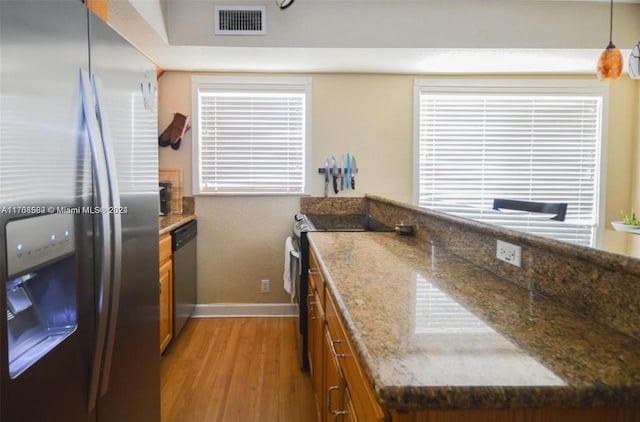 kitchen featuring light hardwood / wood-style flooring, stainless steel appliances, hanging light fixtures, and dark stone counters