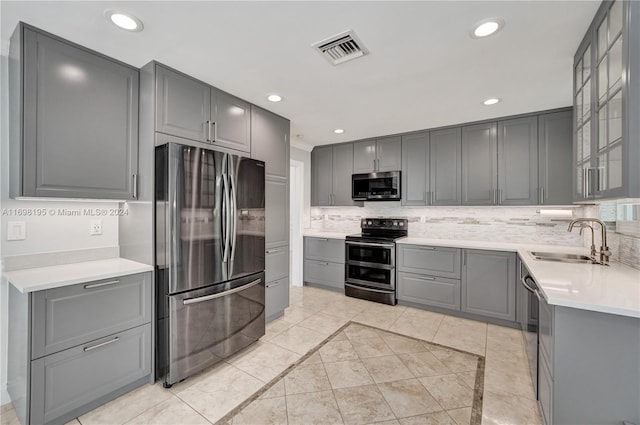 kitchen featuring sink, backsplash, gray cabinets, light tile patterned floors, and appliances with stainless steel finishes