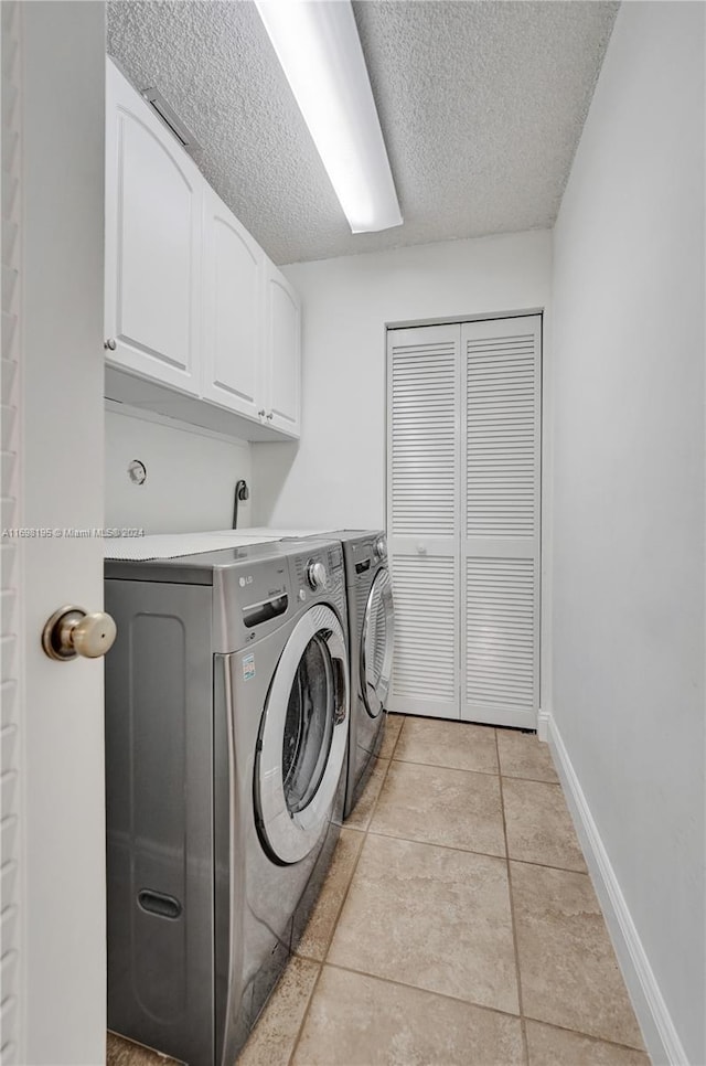 laundry room featuring washer and dryer, light tile patterned flooring, cabinets, and a textured ceiling