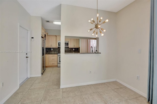 kitchen with light tile patterned flooring, kitchen peninsula, a notable chandelier, and tasteful backsplash