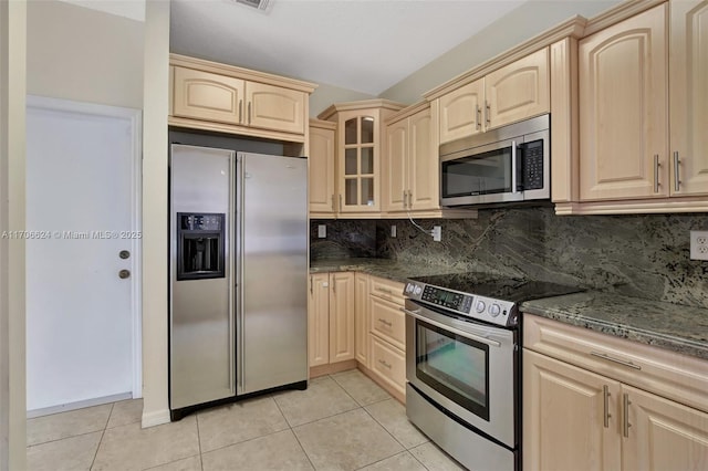 kitchen featuring tasteful backsplash, light tile patterned floors, appliances with stainless steel finishes, and dark stone countertops