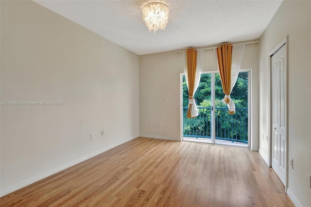 unfurnished room with a textured ceiling, light wood-type flooring, and an inviting chandelier