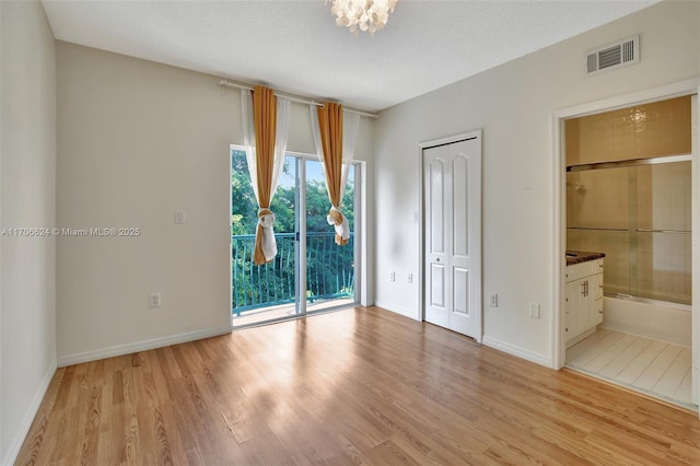 unfurnished bedroom with a textured ceiling, light hardwood / wood-style floors, access to exterior, a closet, and ensuite bathroom