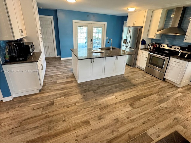 kitchen featuring sink, wall chimney exhaust hood, a kitchen island with sink, white cabinets, and appliances with stainless steel finishes