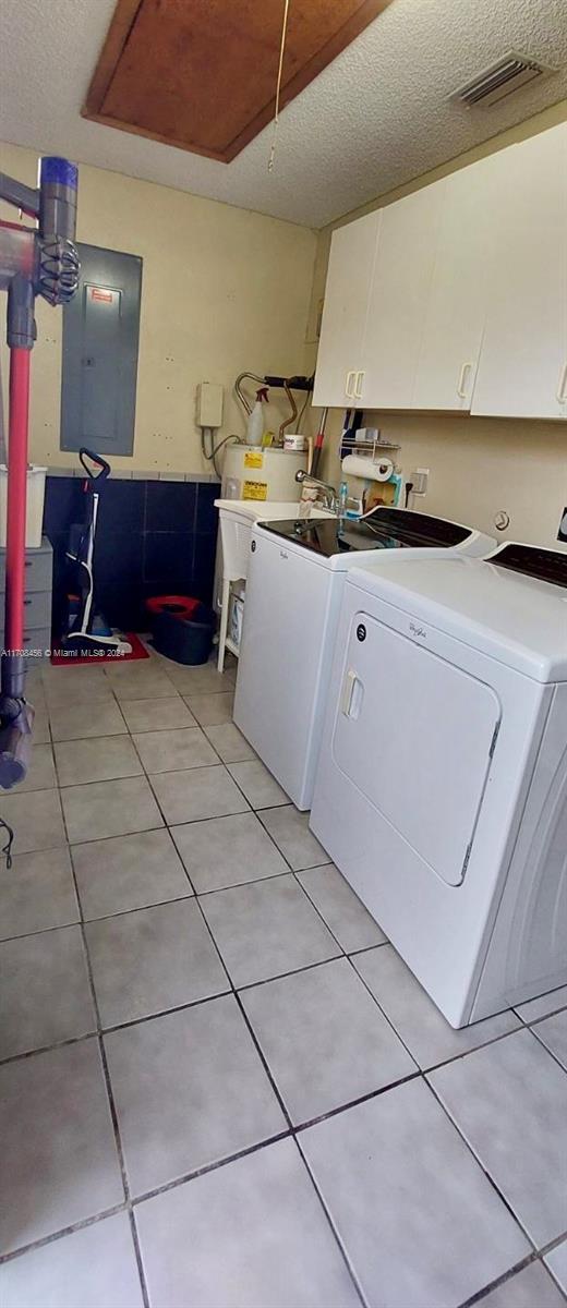 laundry room featuring cabinets, electric panel, light tile patterned floors, separate washer and dryer, and a textured ceiling