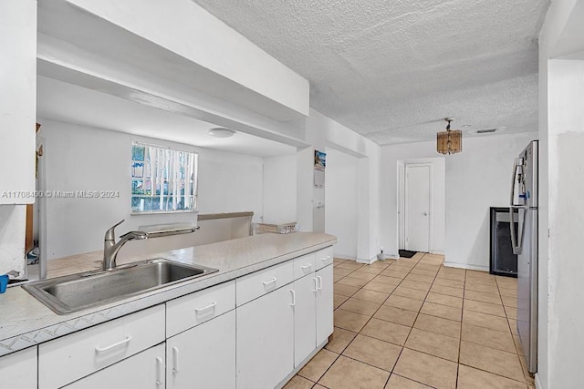 kitchen featuring light tile patterned floors, a textured ceiling, white cabinetry, and sink