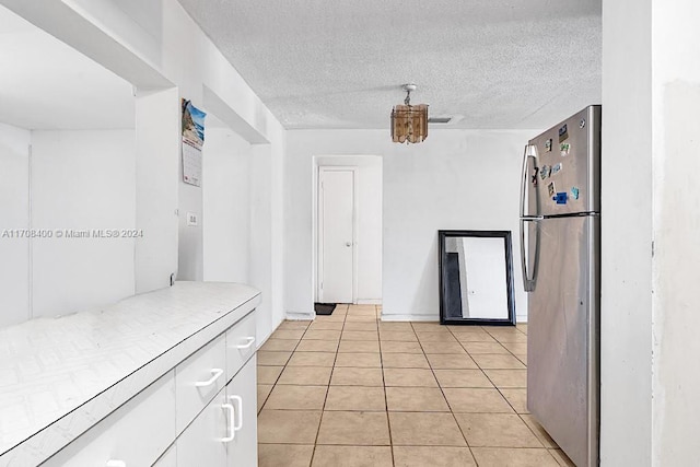 kitchen featuring white cabinets, light tile patterned floors, a textured ceiling, and stainless steel refrigerator