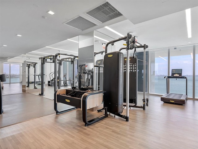 exercise room with expansive windows, a water view, and light hardwood / wood-style floors