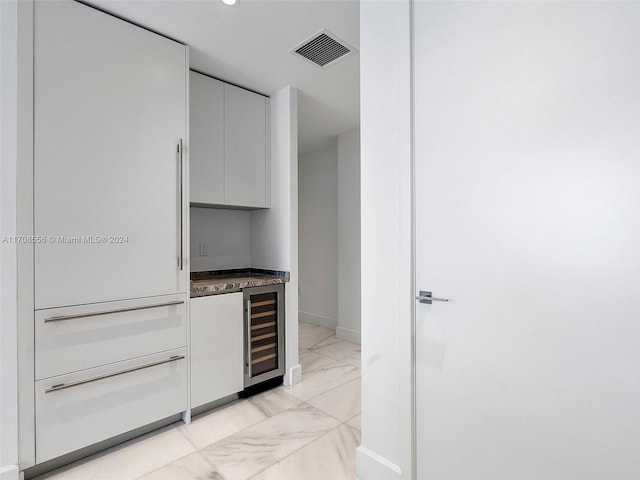 bar featuring white cabinets, dark stone countertops, and beverage cooler