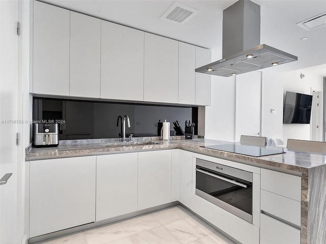 kitchen featuring stainless steel oven, sink, black electric cooktop, island range hood, and white cabinetry