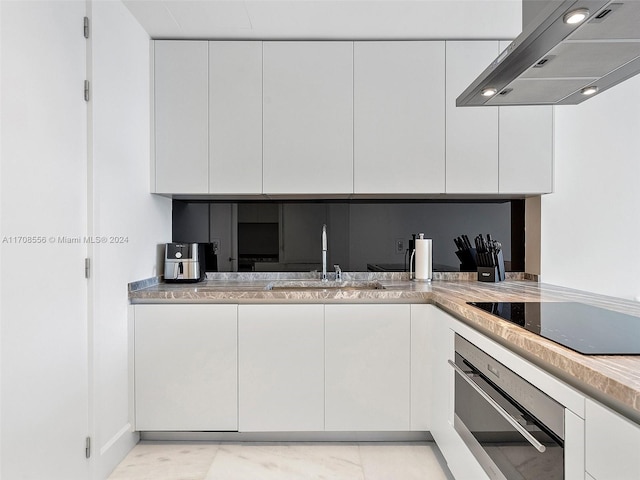 kitchen featuring black electric stovetop, oven, wall chimney range hood, sink, and white cabinetry