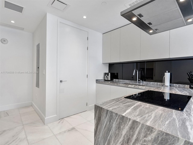 kitchen featuring white cabinets, light stone counters, range hood, and black stovetop