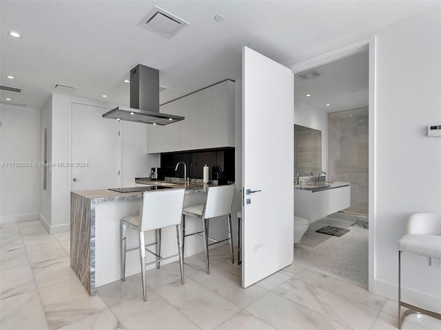 kitchen with island range hood, white cabinetry, a breakfast bar area, and sink