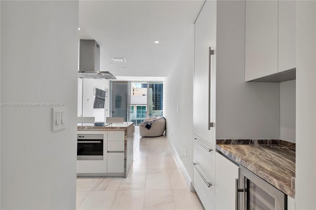 kitchen featuring wall chimney exhaust hood, white cabinetry, oven, wine cooler, and black stovetop