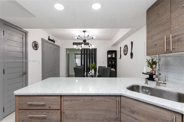 kitchen featuring decorative backsplash, light stone countertops, sink, and a notable chandelier