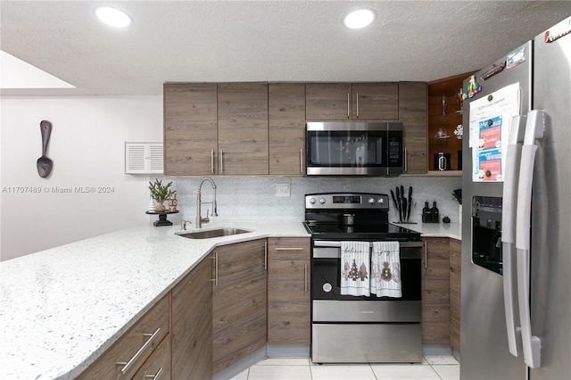 kitchen featuring light stone counters, sink, light tile patterned floors, and stainless steel appliances