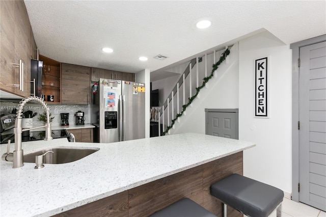 kitchen featuring kitchen peninsula, stainless steel refrigerator with ice dispenser, backsplash, a kitchen breakfast bar, and light tile patterned floors