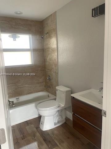 full bathroom featuring hardwood / wood-style floors, tiled shower / bath combo, toilet, and vanity