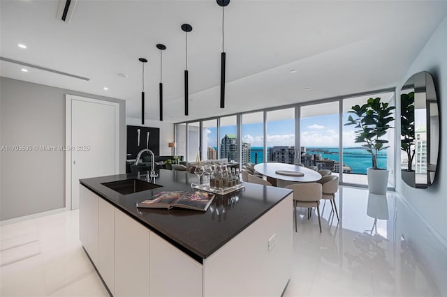 kitchen featuring sink, pendant lighting, white cabinetry, a center island with sink, and expansive windows