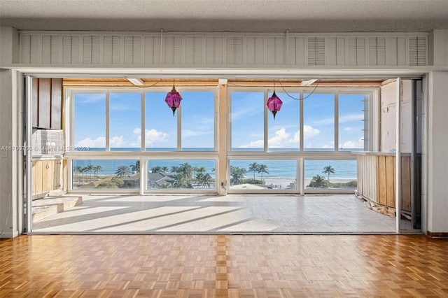 interior space with parquet floors, plenty of natural light, a water view, and a textured ceiling