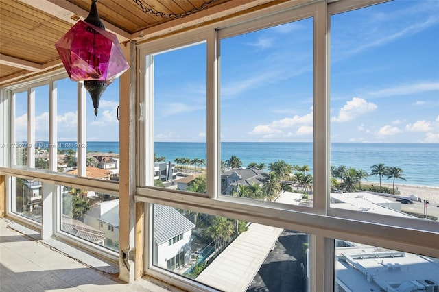 unfurnished sunroom featuring a healthy amount of sunlight, a water view, wood ceiling, and a beach view