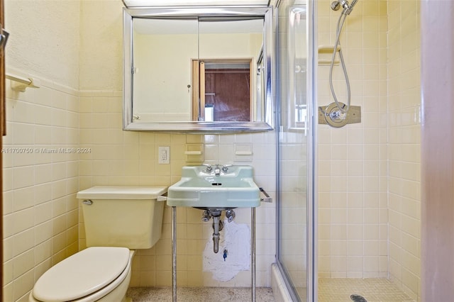 bathroom with a shower with door, toilet, tile walls, and sink