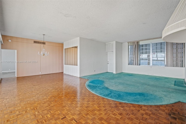 unfurnished room with a textured ceiling, parquet floors, a notable chandelier, and wood walls